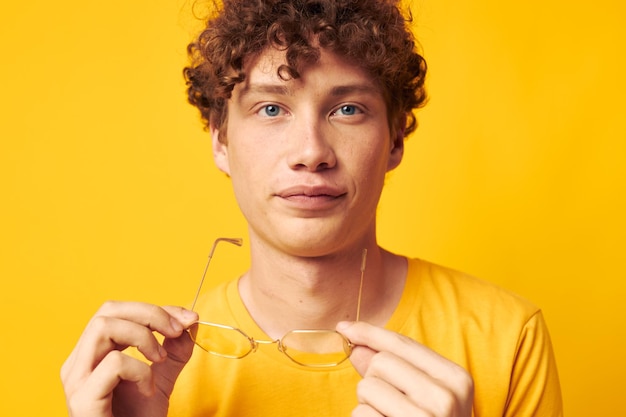 Joven hombre de pelo rizado camiseta amarilla gafas moda gestos con las manos fondo amarillo inalterado