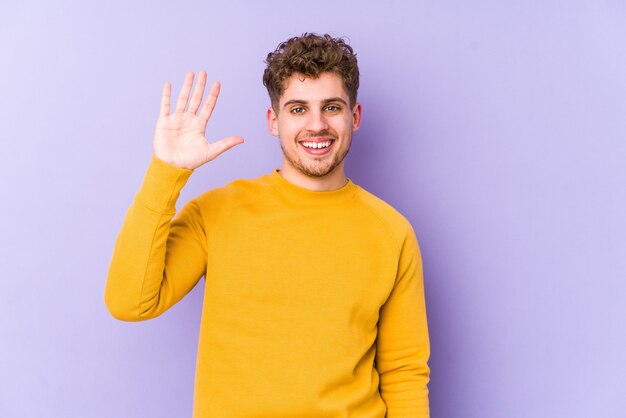 Joven hombre de pelo rizado rubio sonriendo alegre mostrando el número cinco con los dedos