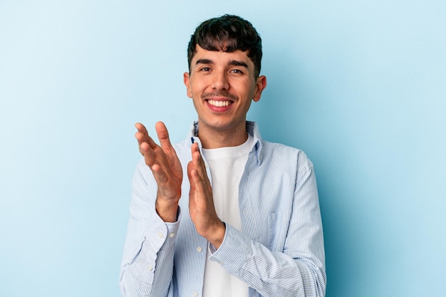 Joven hombre de raza mixta aislado de fondo azul sintiéndose enérgico y cómodo, frotándose las manos con confianza.