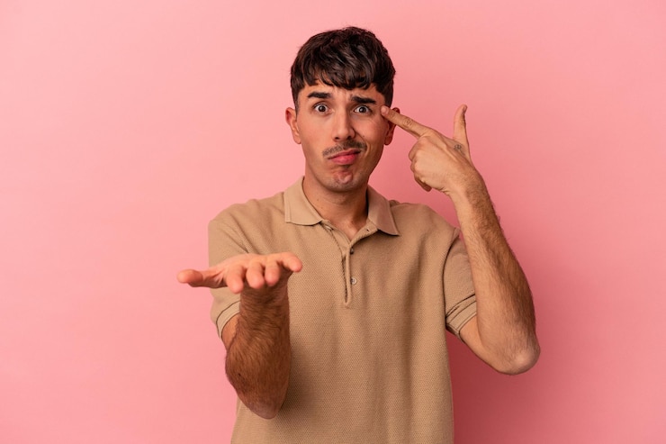 Foto joven hombre de raza mixta aislado de fondo rosa sosteniendo y mostrando un producto a mano.