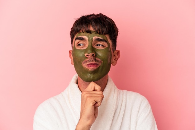 Joven hombre de raza mixta con máscara facial de belleza aislada sobre fondo rosa