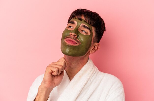 Joven hombre de raza mixta con máscara facial de belleza aislada sobre fondo rosa