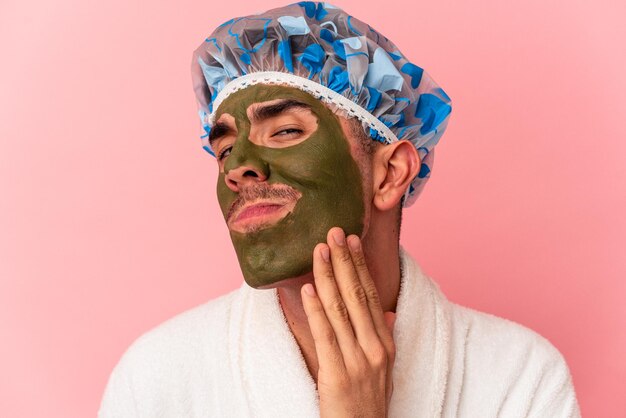 Joven hombre de raza mixta con máscara facial de belleza aislada sobre fondo rosa