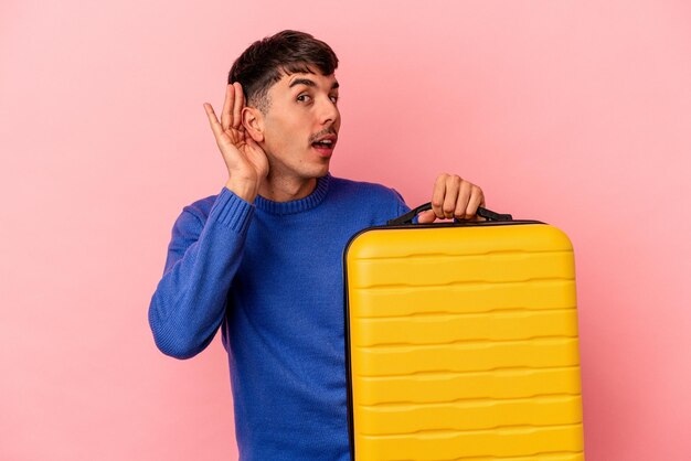 Joven hombre de raza mixta que va a viajar aislado en un fondo rosado tratando de escuchar un chisme.