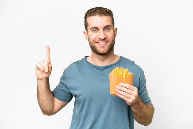 Joven hombre rubio guapo sosteniendo papas fritas sobre un fondo blanco aislado que señala una gran idea