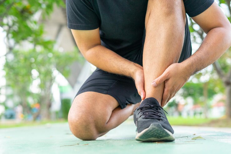 Joven hombre en trajes deportivos negro se lesionó el tobillo durante el ejercicio en el parque Baja sección del deportista que sufre de tobillo volcado mientras estaba sentado en la pista Durante el accidente del concepto de ejercicio