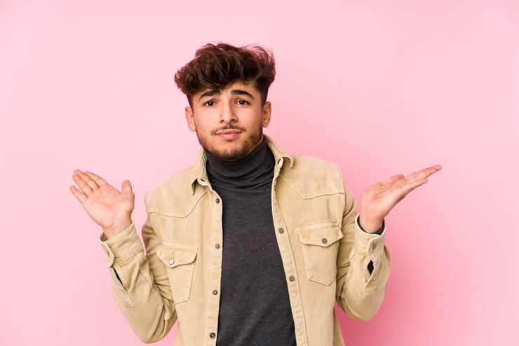 Foto joven ian hombre posando en una pared dudando y encogiéndose de hombros en gesto de cuestionamiento.