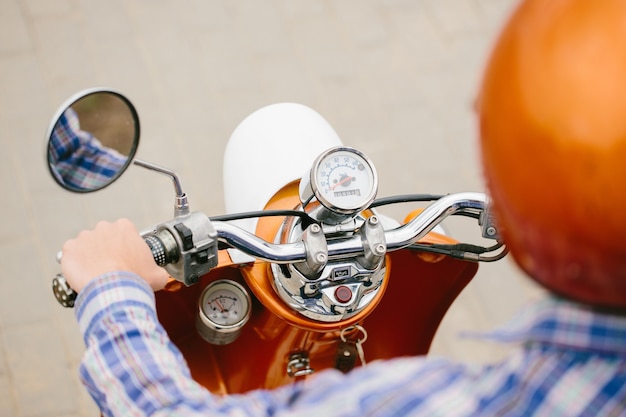 Joven inconformista en casco está montando en scooter retro amarillo en la ciudad