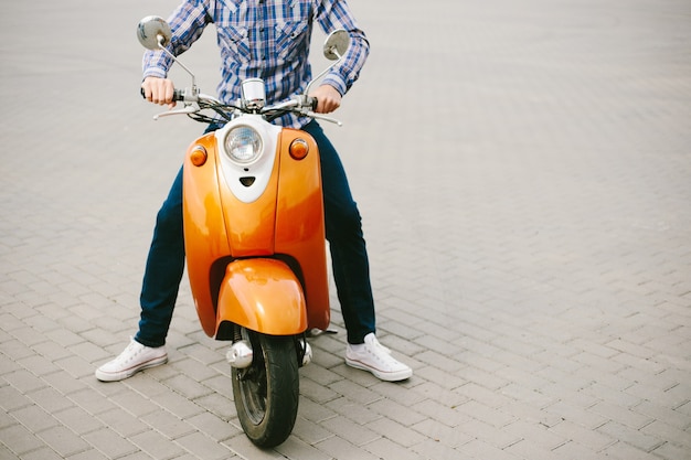 Joven inconformista en casco está montando en scooter retro amarillo en la ciudad
