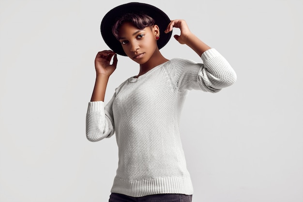 Joven inconformista hermosa chica negra en suéter blanco y sombrero