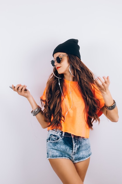 Joven inconformista hermosa mujer con gafas de sol con sombrero negro y camiseta naranja