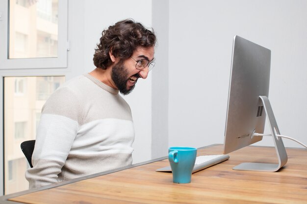 Joven independiente barbudo loco trabajando con su computadora