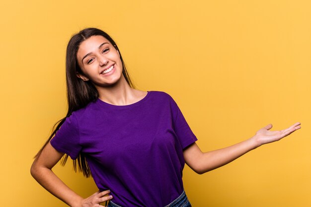 Joven india aislada en amarillo mostrando una expresión de bienvenida.