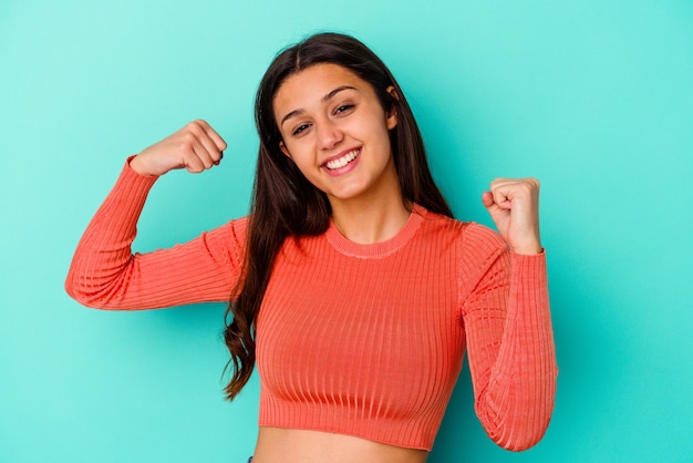 Joven india aislada en la pared azul mostrando gesto de fuerza con los brazos, símbolo del poder femenino