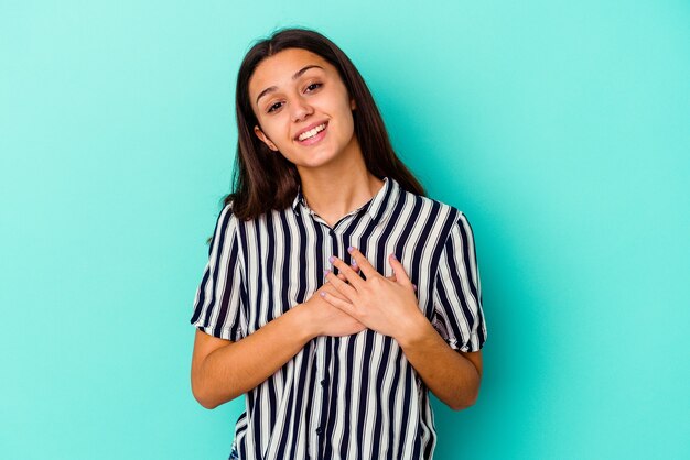 La joven india aislada en la pared azul tiene una expresión amistosa, presionando la palma contra el pecho. Concepto de amor.