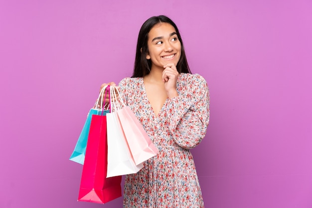 Joven India aislada en púrpura sosteniendo bolsas de compras y pensando