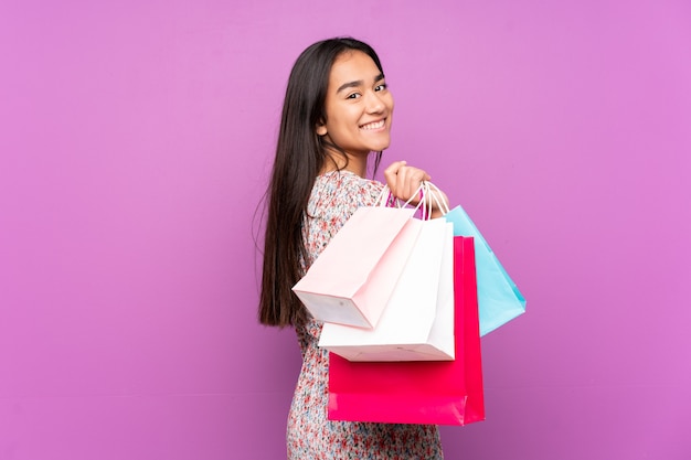 Joven India aislada en púrpura sosteniendo bolsas de compras y sonriendo