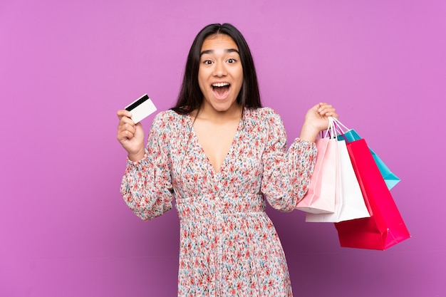 Joven India aislada en púrpura sosteniendo bolsas de compras y sorprendido