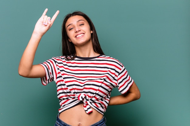 Joven India aislada sobre fondo azul mostrando gesto de rock con los dedos