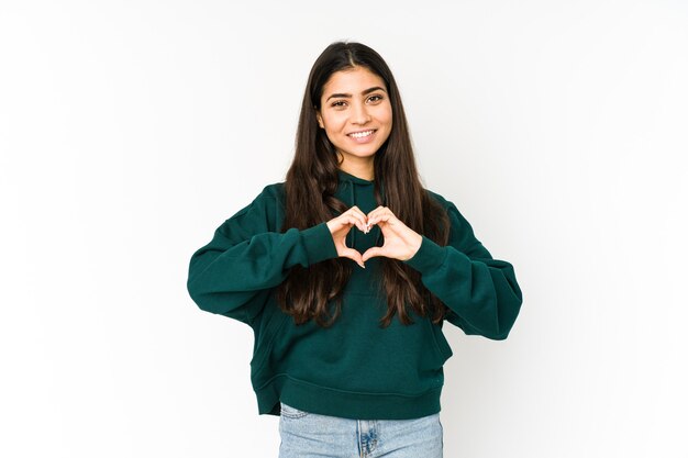 Joven india aislada sobre fondo púrpura sonriendo y mostrando una forma de corazón con las manos.