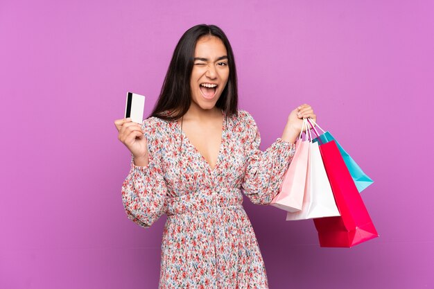 Joven india aislada sobre fondo púrpura sosteniendo bolsas de la compra y una tarjeta de crédito