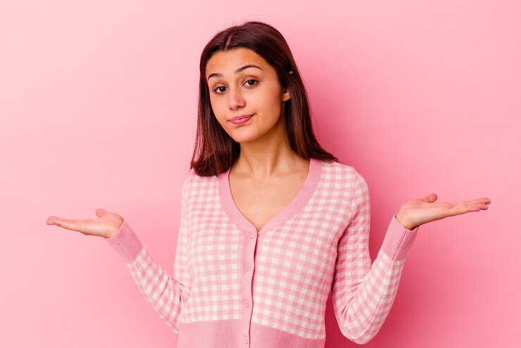 Foto joven india aislada sobre fondo rosa confundido y dudoso encogiéndose de hombros para mantener un espacio de copia.
