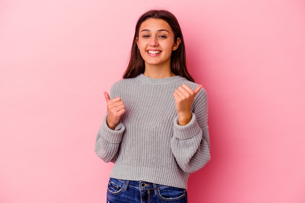 Joven india aislada sobre fondo rosa levantando ambos pulgares, sonriente y confiada.