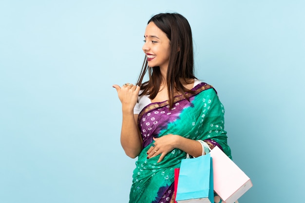 Joven india con bolsas de compras apuntando hacia un lado para presentar un producto