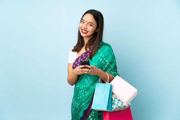 Joven india con bolsas de compras enviando un mensaje con el móvil