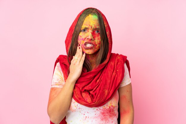 Joven india con coloridos polvos de holi en la cara en la pared rosa con dolor de muelas