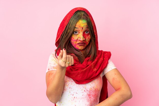 Joven india con coloridos polvos de holi en la cara en la pared rosa haciendo gesto italiano