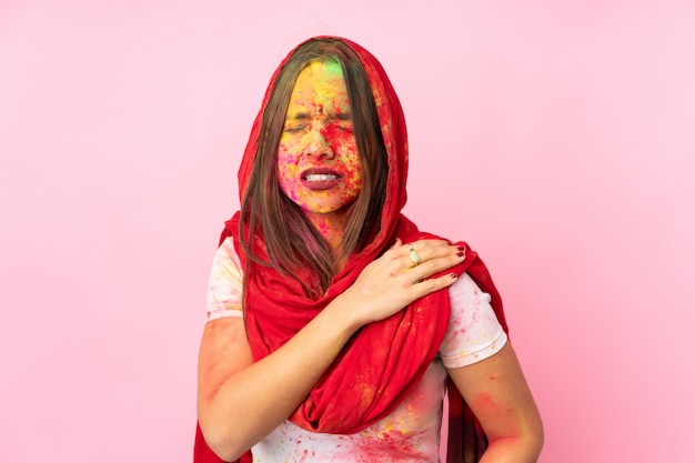 Joven india con coloridos polvos de holi en la cara en la pared rosa que sufre de dolor en el hombro por haber hecho un esfuerzo