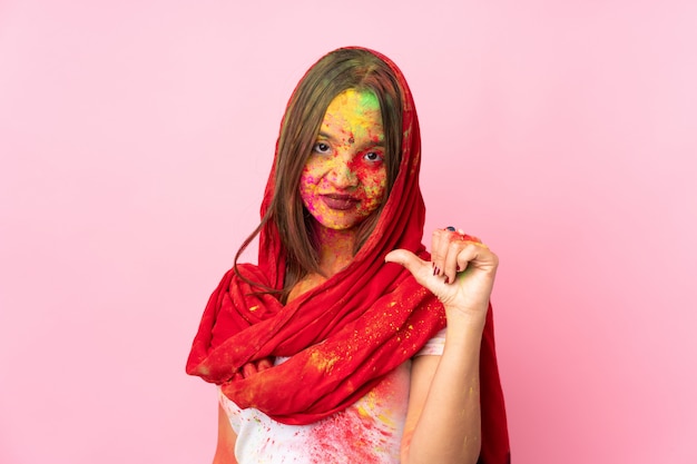 Joven india con coloridos polvos de holi en la cara en la pared rosada orgullosa y satisfecha