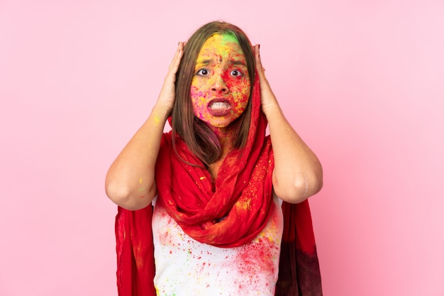 Joven india con coloridos polvos de holi en su rostro aislado en la pared rosa haciendo gesto nervioso