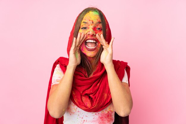 Joven india con coloridos polvos de holi en su rostro aislado en la pared rosa