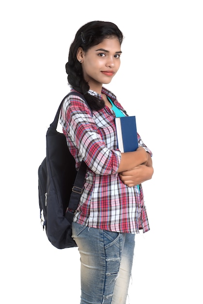 Joven india con mochila de pie y sosteniendo cuadernos, posando sobre un fondo blanco.