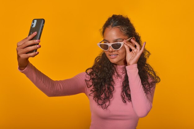 Una joven india se pone gafas de sol en los ojos y se toma una selfie con el teléfono móvil