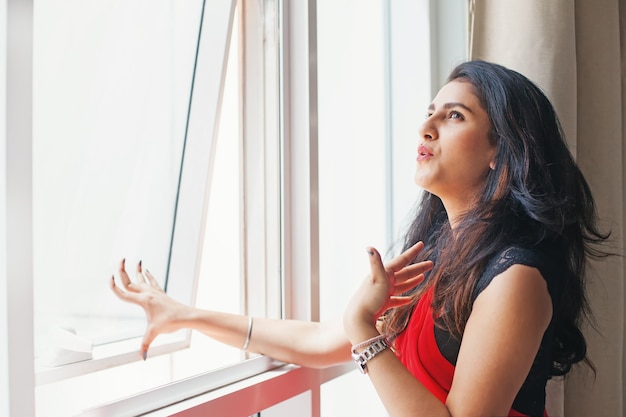 Joven india en sari abriendo la ventana debido al calor extremo del verano