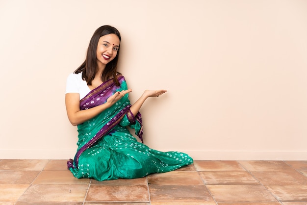 Foto joven india sentada en el suelo extendiendo las manos hacia un lado para invitar a venir