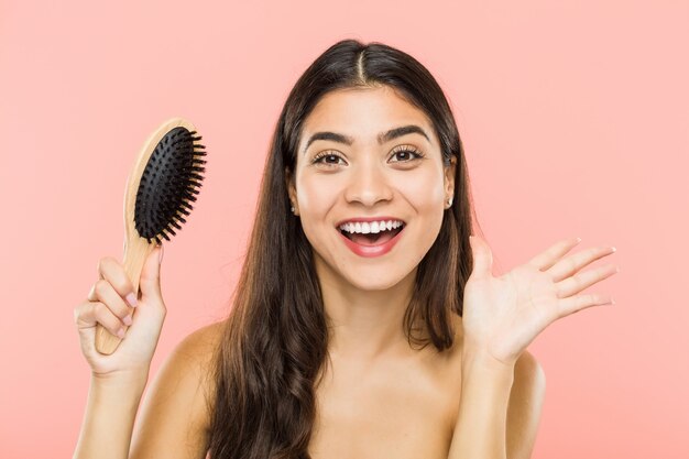 Joven india sosteniendo un cepillo para el pelo celebrando una victoria o éxito