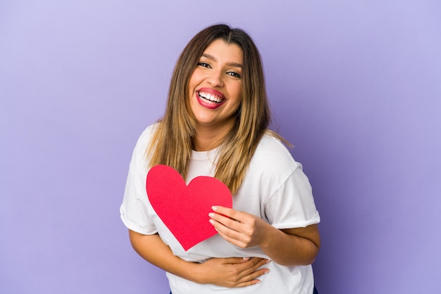 Joven india sosteniendo un corazón de San Valentín aislado riendo y divirtiéndose.