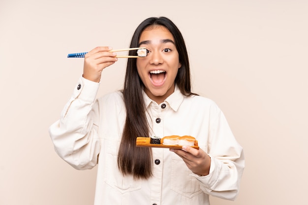 Joven india sosteniendo sushi en pared beige