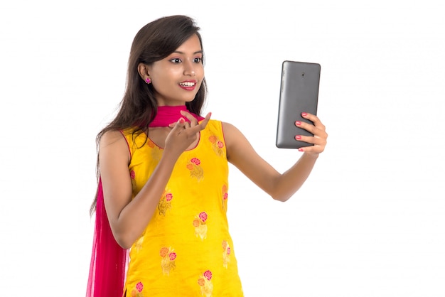 Joven india usando una tableta, teléfono móvil o teléfono inteligente aislado sobre un fondo blanco.