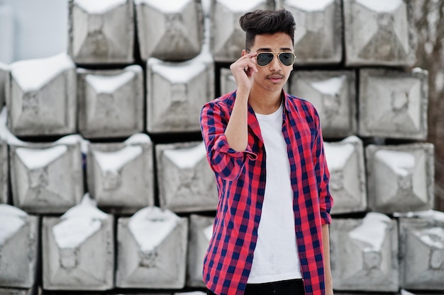 Un joven indio casual con camisa a cuadros y gafas de sol posó contra bloques de piedra