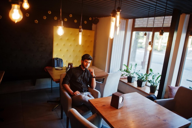 Joven indio confiado con camisa negra sentado en el café