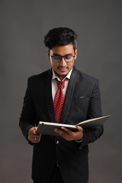 Joven indio exitoso hombre de negocios o ejecutivo con gafas y leyendo un libro sobre un fondo oscuro.