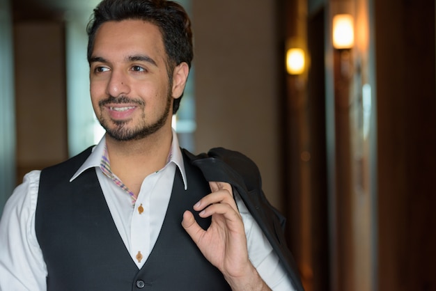 Foto joven indio feliz sonriendo mientras sostiene la chaqueta y apartar la mirada en los pasillos del hotel