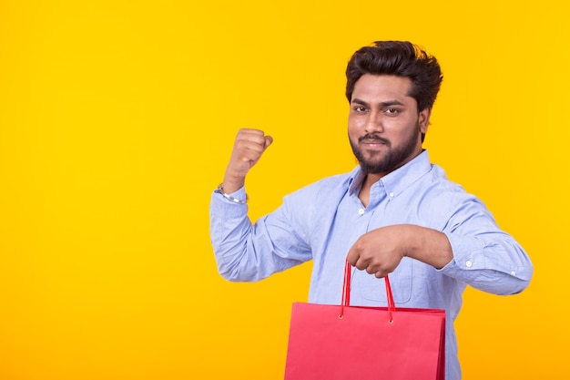 Joven indio guapo con barba sostiene bolsas rojas posando en una pared amarilla