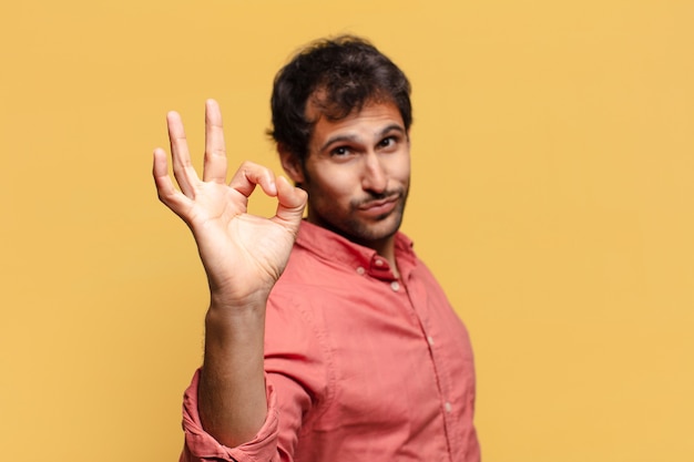 Joven indio guapo con expresión feliz y sorprendida haciendo el signo de ok