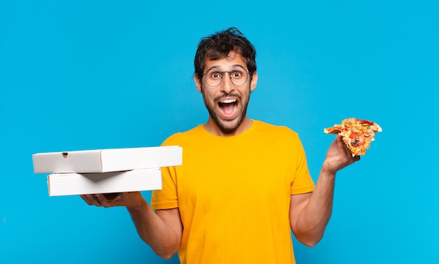 Joven indio guapo sorprendido expresión y sosteniendo pizzas para llevar